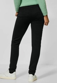 Svarta avsmalnande byxor i en texturerad tyg, elastisk midja, två bakfickor och ribbade anklar, kombinerat med vita sneakers.