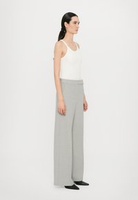 Grå vide bukser med en glat tekstur og en skræddersyet pasform, parret med en tætsiddende hvid tanktop. Enkel design, ingen mønstre eller hardware.