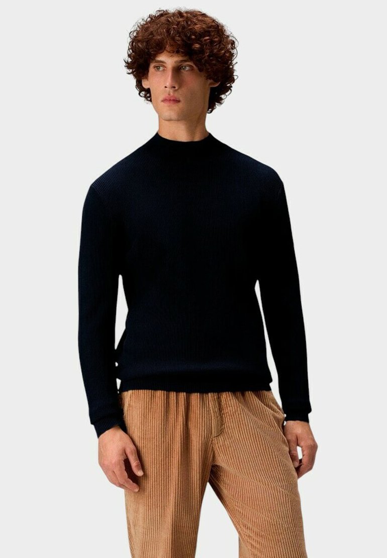 Marineblauer gerippter Pullover mit Stehkragen, langen Ärmeln und figurbetontem Schnitt, kombiniert mit hellbraunen Cordhosen mit vertikalen Streifen.