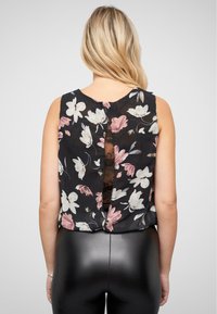 Top senza maniche floreale con sfondo nero, caratterizzato da fiori rosa e bianchi. Sul retro presenta un dettagliato taglio in pizzo. Tessuto morbido e vestibilità comoda.