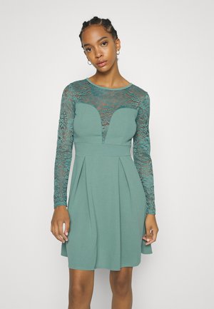 Um vestido azul-turquesa com um corpete justo, mangas longas em renda e uma saia rodada. A gola apresenta um recorte em forma de coração.