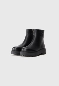 Bottines en cuir noir avec semelles en caoutchouc épaisses, fermeture éclair latérale et logo DKNY embossé sur la cheville extérieure.