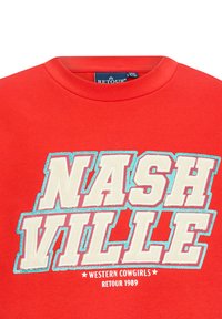 Felpa rossa con grande testo bianco e blu che recita "NASHVILLE" con un effetto invecchiato, e "WESTERN COWGIRLS RETOUR 1989" sottostante.