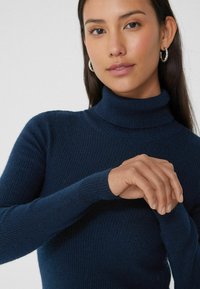 Pull à col roulé côtelé bleu marine avec des manches longues et une coupe ajustée, présentant une texture lisse sans motifs ni embellissements visibles.