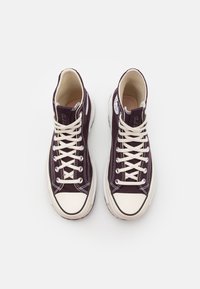 Wysokie trampki w ciemnofioletowym płótnie z kremowymi sznurówkami, gumowymi noskami i białymi podeszwami. Posiadają metalowe oczka i detale podszewki.