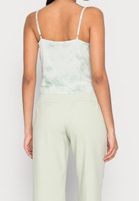 Jasnozielony top na ramiączkach z efektem tie-dye, widziany od tyłu, w komplecie z dopasowanymi jasnozielonymi spodniami. Gładka faktura, casualowy design.