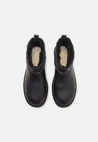 Botas de tobillo de cuero negro con un forro suave en color crema, puntera redonda y cremallera lateral. Las características incluyen costuras en contraste y lengüetas para facilitar el calzado.
