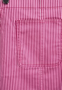 Tejido a rayas diagonales en rosa y blanco que presenta un bolsillo frontal con costura superior y herrajes de botón metálico. Material suave y texturizado.