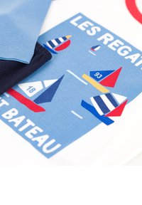 T-shirt con una grafica di barche a vela colorate su uno sfondo blu. Il design include accenti rossi, blu e gialli, con testo bianco.