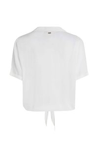 Blusa blanca de manga corta hecha de material ligero, con cuello y detalle de lazo en la parte trasera, con una textura lisa y uniforme.