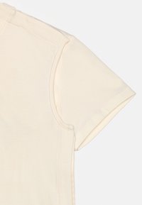 Sectie van een crèmekleurig T-shirt met korte mouwen, waarbij de gestikte mouwnaad en het geribde stofdetail zichtbaar zijn op een vlakke lichte achtergrond.