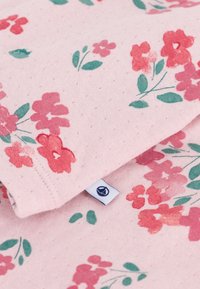 Tessuto rosa con un motivo testurizzato che presenta fiori rossi e rosa, foglie verdi e una piccola etichetta nell'angolo in basso.