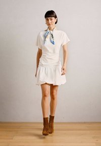 Vestido blanco con mangas cortas y falda fruncida, combinado con una bufanda de seda azul claro y floral, y botines marrones. Tela suave y forma acampanada.