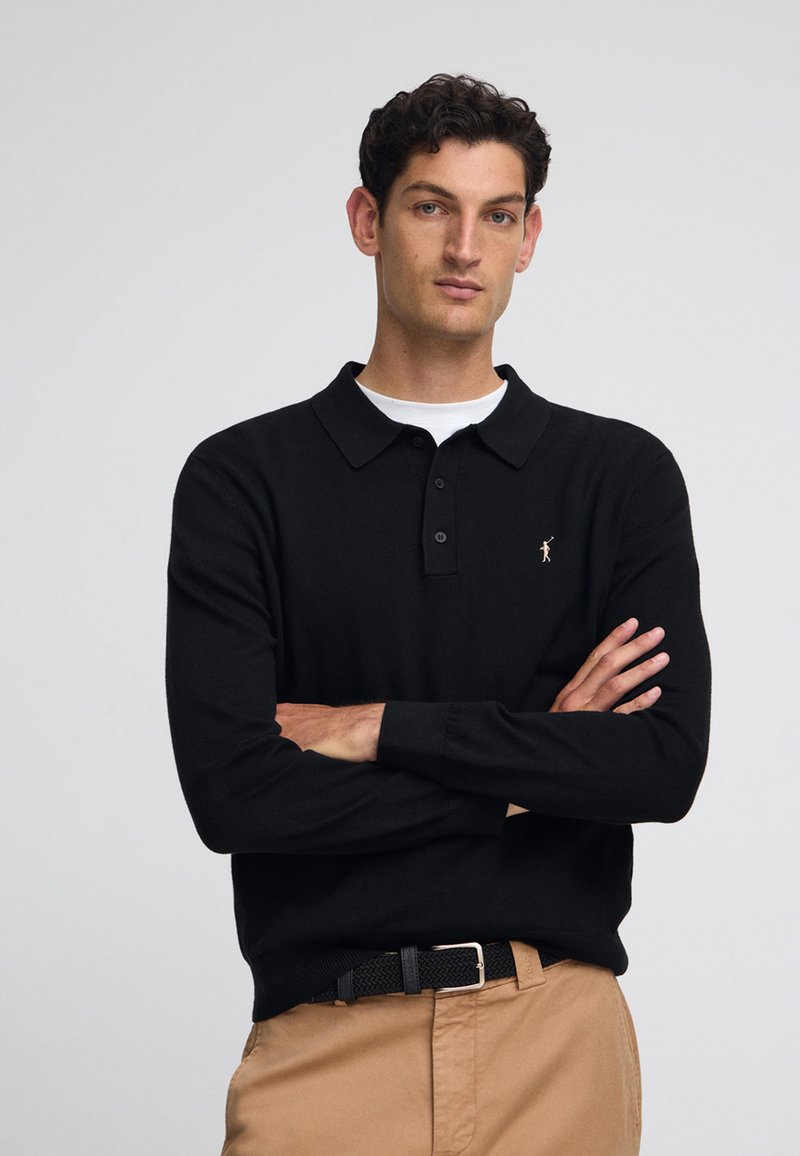 Svart långärmad polo med krage och treknapplåsning. Har en liten broderad detalj på bröstet och ribbade muddar.
