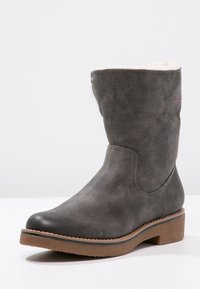 Bottine grise en cuir synthétique avec une doublure douce et pelucheuse, un bout rond et une surface texturée. Elle présente un petit talon bloc et des détails cousus.