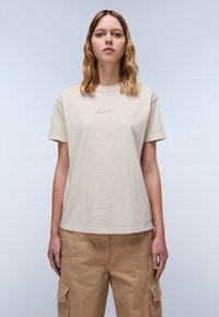 Beige katoenen t-shirt met korte mouwen en een ronde hals, met geborduurd "NAPA" in een subtiele tint, gecombineerd met losse kaki cargopants.