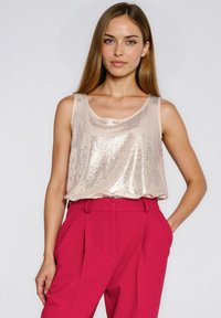 Top bez rękawów z cekinami w jasnoróżowym odcieniu z dekoltem w serek, zestawiony z wysokim stanem jasnoróżowych spodni o szerokich nogawkach i kieszeniach.