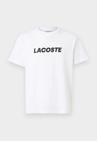 Balta medvilninė marškinėliai su ryškiu juodu "LACOSTE" logotipu ant krūtinės. Trumpomis rankovėmis ir apvalia iškirpte.