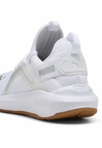 Zapatilla deportiva blanca con parte superior de malla texturizada, talón acolchado y suela de goma. Presenta un logo de PUMA en gris y una lengüeta para facilitar el calzado.