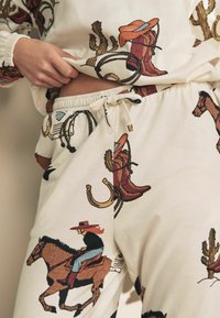 Set de îmbrăcăminte de relaxare din bumbac cu un fundal crem și motive occidentale vibrante, inclusiv cizme, lațuri și cowboys. Talie elastică.