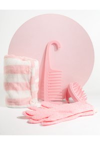 En rosa och vit randig handduk, en rosa utredningskam, en rosa hårbottenmassager och exfolierande handskar arrangerade med en rosa cirkulär bakgrund.