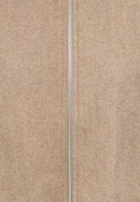 Beige wool fabric with a centered silver metal zipper, partially zipped, showing texture and stitch details.