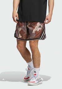 Kratke hlače u smeđoj i bež kamuflažnoj boji s crnim detaljima i bočnim prugama. Lagani materijal, dužine do koljena, s elastičnim pojasom i opuštenim krojem.