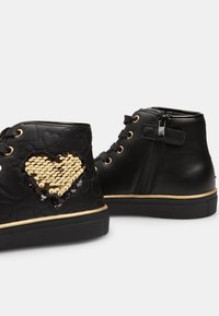 Des chaussures montantes noires avec un design en sequins dorés et noirs en forme de cœur, en cuir texturé, avec des accents dorés et une fermeture éclair sur le côté.