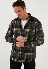 Cămașă din flanel cu un model în carouri verde, bleumarin și galben, cu mâneci lungi, închidere cu nasturi și croială lejeră.