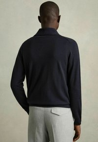 Suéter de manga larga en color navy con cuello, que presenta una textura suave. Se muestra con pantalones en gris claro en un entorno neutro.