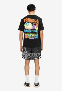 Zwart T-shirt met meerkleurige grafische tekst op de achterkant, gecombineerd met zwarte shorts met een wit paisleypatroon en contrasterende bies.
