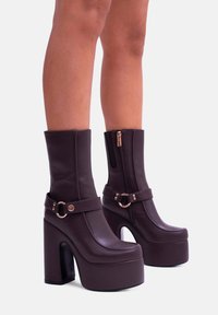 Stivali platform viola realizzati in materiale sintetico liscio, con tacco alto, gambale largo, cerniera frontale e una fascia con un accento circolare.