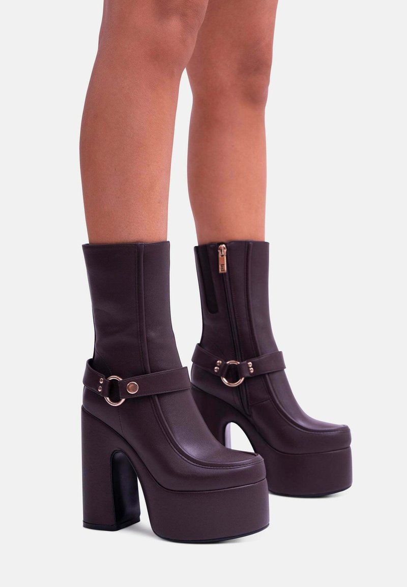 Stivali platform viola realizzati in materiale sintetico liscio, con tacco alto, gambale largo, cerniera frontale e una fascia con un accento circolare.