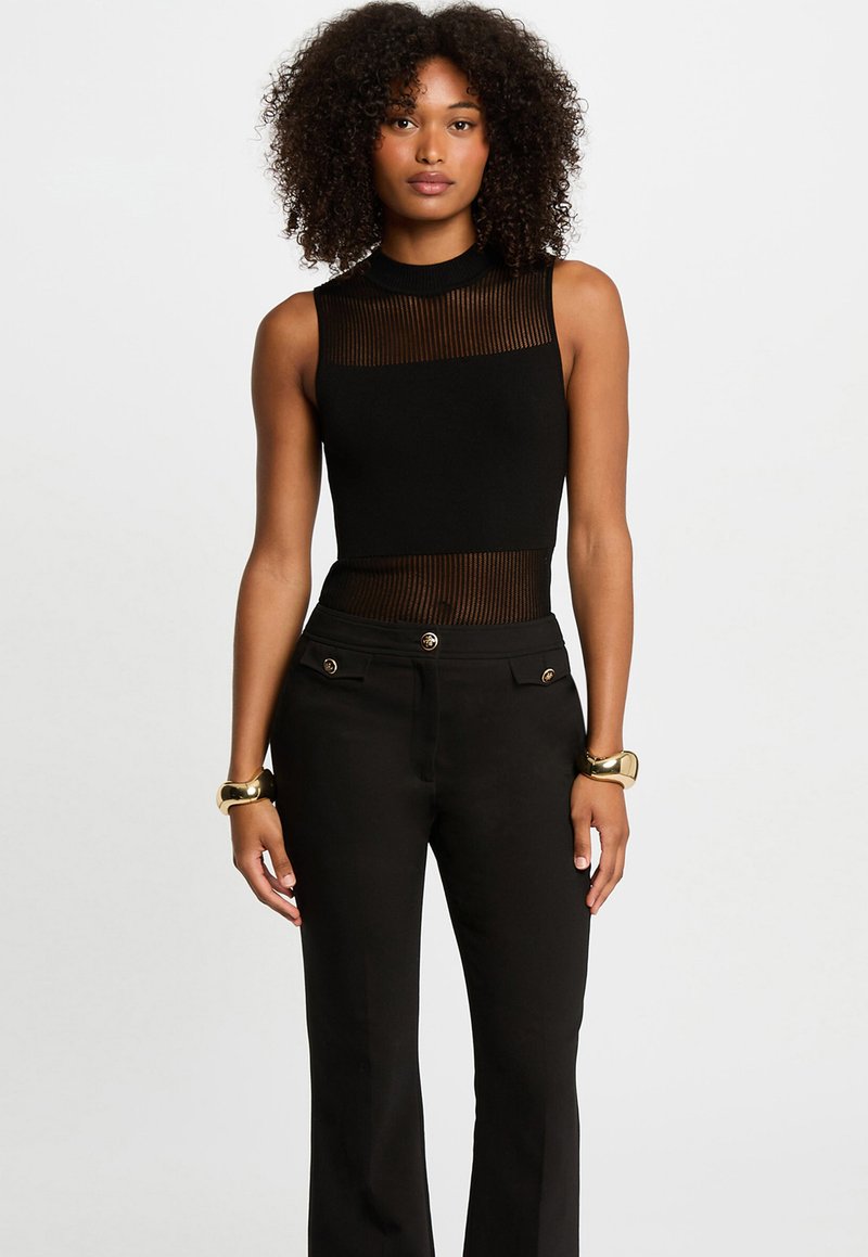 Haut sans manches noir avec un col montant et un design en maille rayée transparente. Associe à un pantalon noir taille haute avec des accents de boutons dorés.