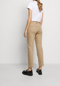 Pantalones de algodón beige con corte recto, que cuentan con bolsillos traseros y costuras en contraste. Combinados con unos zapatos negros sin cordones.