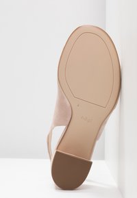 Chaussure à talon haut en suède nude avec un nez arrondi, des côtés ouverts et une semelle en caoutchouc brun texturé avec le nom de la marque en relief.