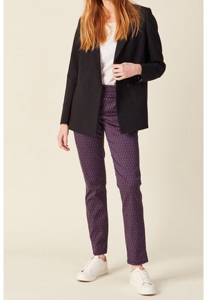 Černý blazer přes bílý tričko, doplněný o vzorované fialové kalhoty a bílé tenisky. Má upravený střih a texturovanou tkaninu.
