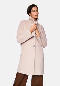 Helle rosa Wolljacke mit hohem Kragen, einer schwarzen Knopfverschlüsse, seitlichen Taschen und einer lockeren Passform. Glatte Textur, modernes Design.