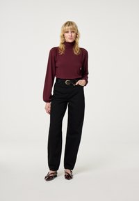 Bordeauxkleurige langesleeve coltrui, gecombineerd met hoge zwarte broeken en donkere versierde flats. Eenvoudige riemdetails, gladde stoftextuur.
