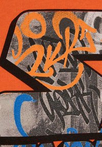Arte grafica con vernice spray arancione brillante, blu e nera su tessuto texturizzato, con forme abstracte e lettering audaci.