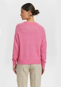 Rausvos megztos palaidinės minkšta tekstūra, su pūkuotais rankogaliais ir apatine dalimi. Dizainas turi apvalų iškirpimą ir raglan tipo rankoves. Suderinta su kreminiais kelnių.