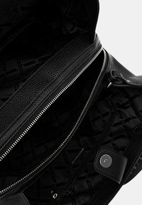 Interno di una borsa in pelle nera con scomparto a zip, chiusura a bottone magnetico e fodera in tessuto decorato. Materiale testurizzato.