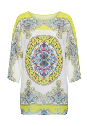 Biała i żółta bluzka z długim rękawem z misternymi kwiatowymi i geometrycznymi wzorami w kolorach niebieskim, różowym i zielonym na przodzie i rękawach.