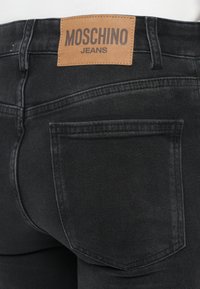Crne traperice od denima s kožnom oznakom Moschino na pojasu, stražnjim džepovima s kontrastnim šavovima i suženim krojem.