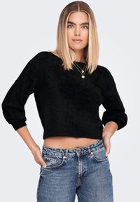 Black, fuzzy crop sweater with a round neckline and three-quarter sleeves, paired with high-waisted, light-wash denim jeans.