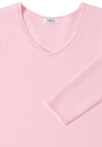 Pull texturé rose clair à manches longues avec encolure en V et bordure blanche sur le col et le poignet, avec une étiquette de marque "CECIL".