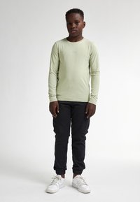 Lichtgroen langemouwen shirt, zwarte cargobroek met zakken, en witte sneakers. Eenvoudig ontwerp met een comfortabele pasvorm.