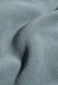 Tissu texturé dans un bleu doux et muted, présentant une surface lisse et légèrement brillante avec de douces plis et contours.
