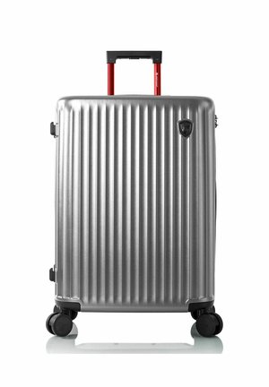Silver hard-shell suitcase with vertical ridges, four black wheels, and a red retractable handle extended.