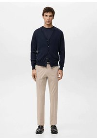 Cárdigan de punto azul marino con escote en V, botones en la parte delantera y mangas largas, combinado con pantalones beige y zapatos negros. Diseño sencillo y ajustado.